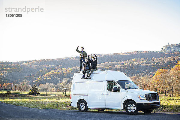 Glückliche Freunde mit erhobenen Armen auf Wohnmobil sitzend