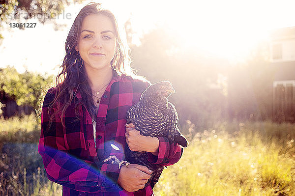Porträt einer Frau  die auf Gras stehend ein Huhn trägt