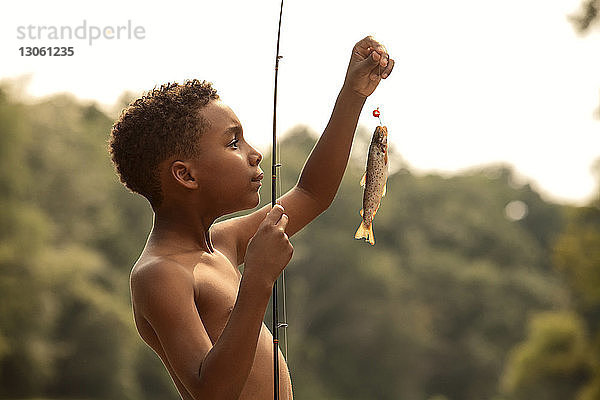 Seitenansicht eines Jungen  der mit der Angelrute gefangene Fische betrachtet