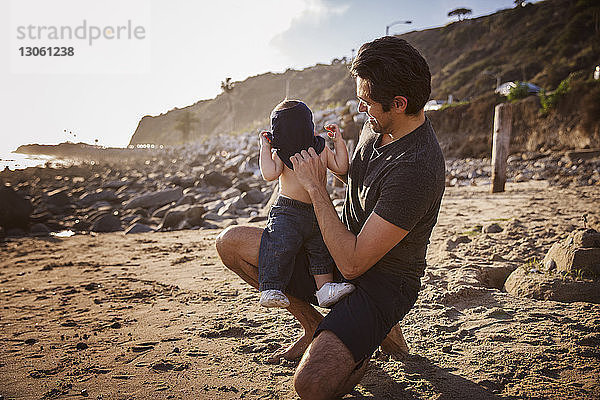 Glücklicher Vater legt seinem Sohn am Strand das Hemd hin