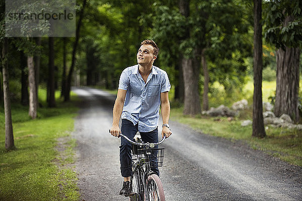 Glücklicher Mann schaut auf  während er auf einer Straße im Wald Fahrrad fährt