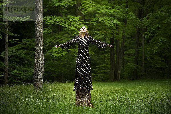 Frau mit ausgestreckten Armen auf Baumstumpf im Wald stehend