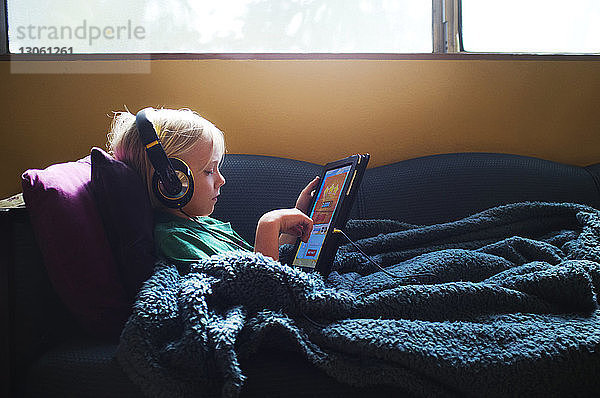 Junge hört Musik  während er am Tablet-Computer auf dem Sofa zu Hause spielt