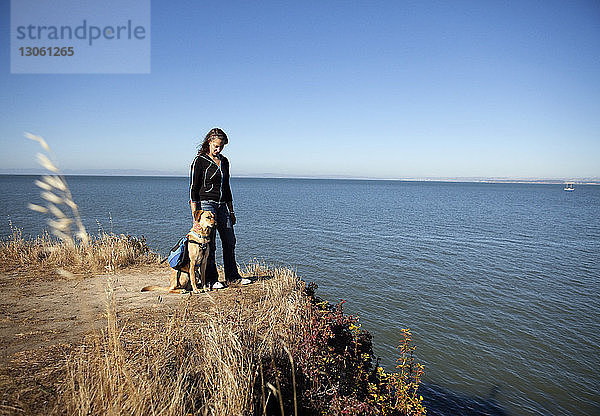 Frau und Hund auf dem Feld gegen Meer und Himmel an einem sonnigen Tag