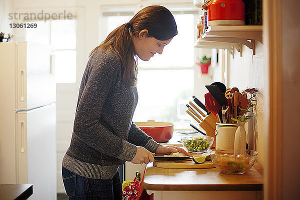 Seitenansicht einer Frau  die zu Hause in der Küche Gemüse auf einem Schneidebrett schneidet