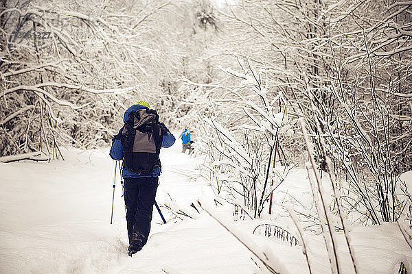 Rückansicht eines männlichen Wanderers mit Rucksack beim Gehen auf schneebedecktem Feld