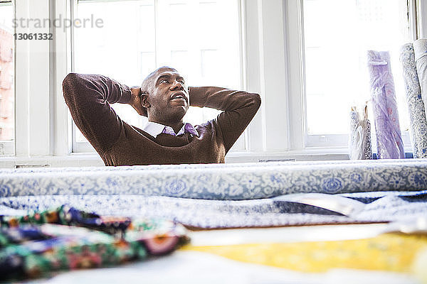 Männlicher Modedesigner entspannt am Schreibtisch gegen das Fenster in einem Workshop