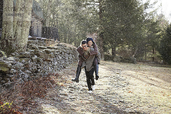 Mann nimmt im Winter seine Freundin im Wald huckepack