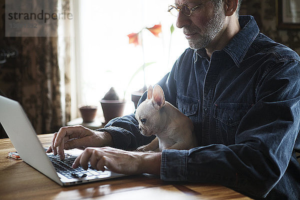 Mann sitzt mit Hund  während er zu Hause einen Laptop benutzt