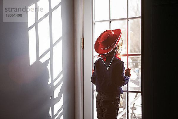 Rückansicht eines Jungen mit Hut  der durch ein Fenster schaut