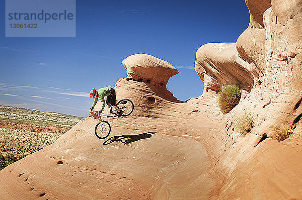 Mountainbiker springen von Klippe gegen blauen Himmel