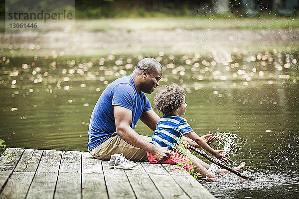 Glückliche Familie spritzt Wasser  während sie auf dem Steg am See sitzt