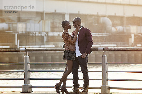 Romantisches Paar in voller Länge an Geländer gegen Fluss stehend
