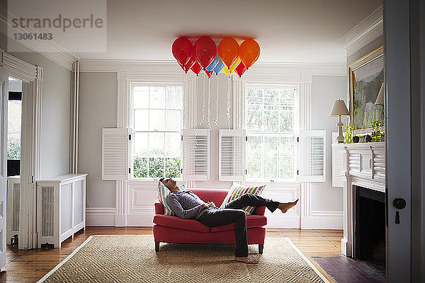 Mann schaut Heliumballons an  während er auf dem Sofa liegt