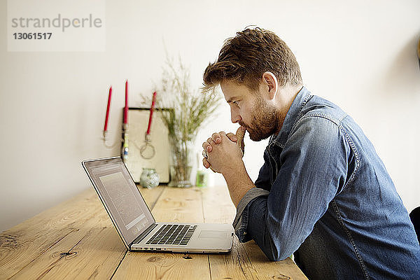 Seitenansicht eines konzentrierten Mannes  der am Tisch sitzend auf den Laptop schaut