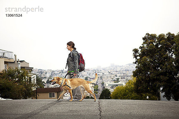 Seitenansicht von Frau und Hund beim Spaziergang auf der Straße gegen das Stadtbild