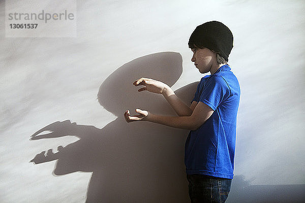 Seitenansicht eines Jungen  der zu Hause mit Schatten an der Wand spielt