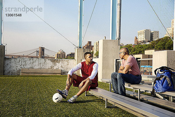 Sohn spricht mit Vater  während er auf der Tribüne eines Fussballfeldes sitzt