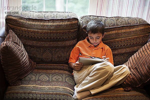 Junge benutzt Tablet-Computer  während er zu Hause auf dem Sofa sitzt