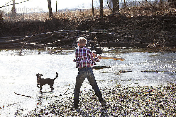 Rückansicht eines Teenagers  der mit einem Hund am Fluss spielt