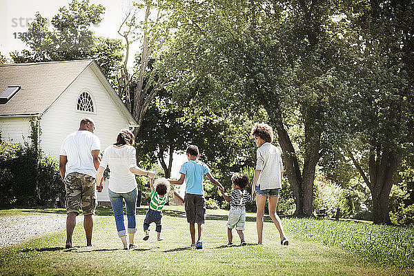 Rückansicht einer Familie  die beim Spaziergang auf einem Grasfeld im Hinterhof Händchen hält