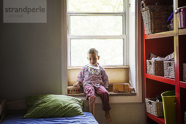 Porträt eines Jungen auf dem Fensterbrett im Schlafzimmer zu Hause