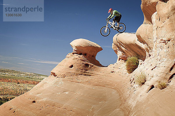 Seitenansicht eines Mountainbikers auf einer Klippe vor blauem Himmel