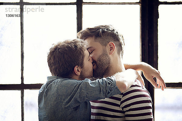 Zärtliches schwules Paar küsst sich zu Hause am Fenster