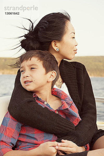 Nachdenkliche Mutter sitzt mit ihrem Sohn im Boot um den Arm
