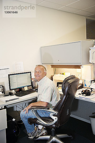 Porträt eines glücklichen reifen Geschäftsmannes  der im Büro am Schreibtisch sitzt