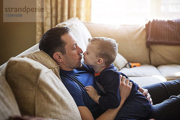 Vater küsst Sohn  während er zu Hause auf dem Sofa sitzt