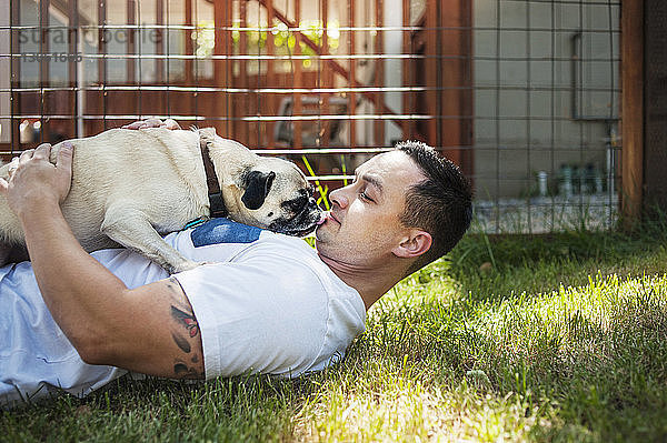 Mann spielt mit Mops auf Grasfeld im Hinterhof