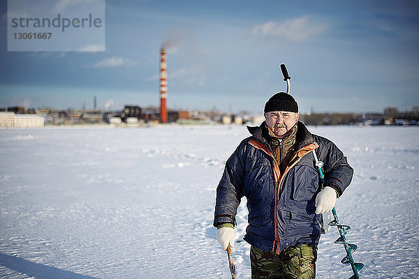 Porträt eines älteren Mannes  der einen Bohrer trägt  während er auf einem zugefrorenen See geht