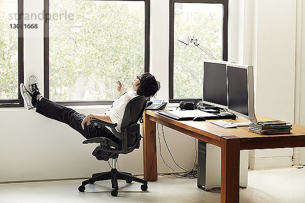 Seitenansicht eines Geschäftsmannes  der sich im Büro auf einem Stuhl entspannt