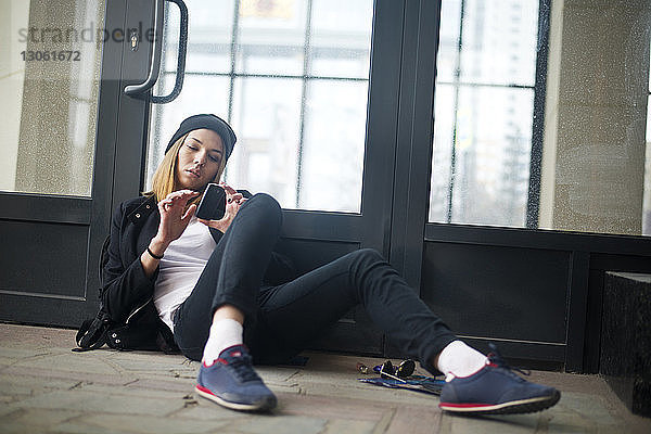 Hipsterin benutzt Telefon  während sie sich vor der Tür entspannt