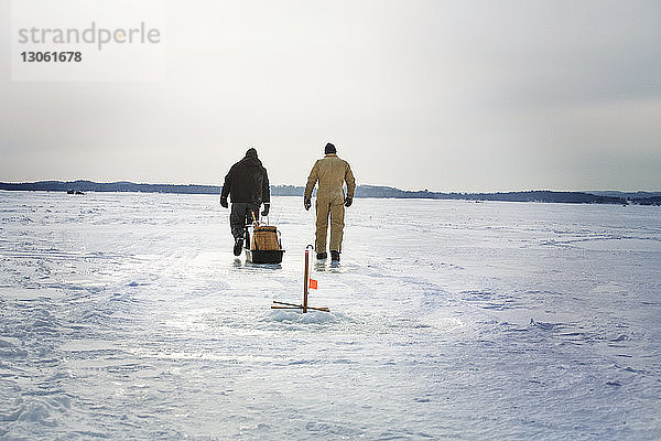 Rückansicht von Freunden  die auf einem zugefrorenen See vor bewölktem Himmel spazieren gehen