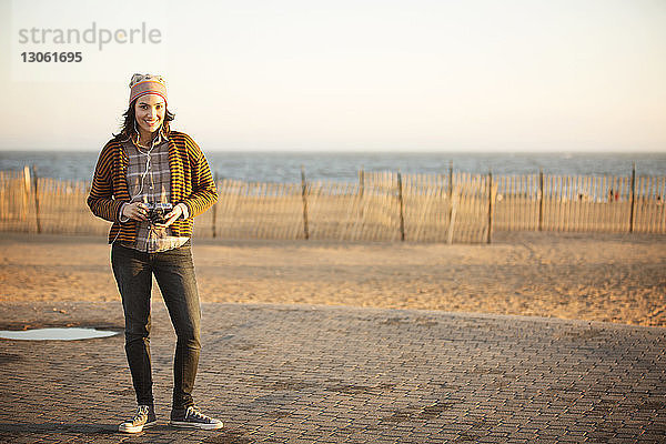 Porträt einer Frau  die eine Digitalkamera hält  während sie auf dem Bürgersteig des Strandes steht