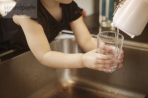 Beschnittenes Bild eines Mädchens  das in der Küche ein Glas Wasser füllt