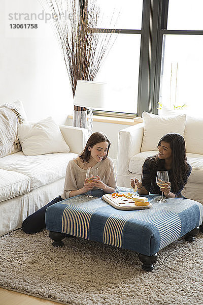 Schrägansicht auf Freunde  die zu Hause Snacks mit Wein genießen  während sie sich entspannen