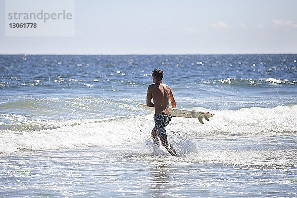 Mann trägt Surfbrett im Meer gegen den Himmel
