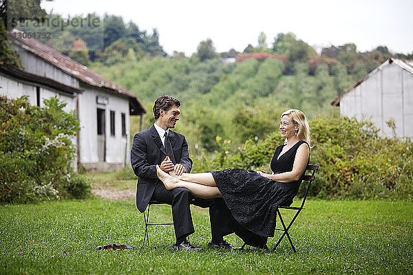 Mann hält Frauenfüsse  während er auf einem Stuhl auf einem Grasfeld sitzt
