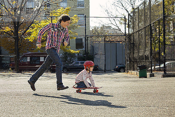 Seitenansicht eines Mannes  der rennt  während sein Sohn im Park Skateboard fährt
