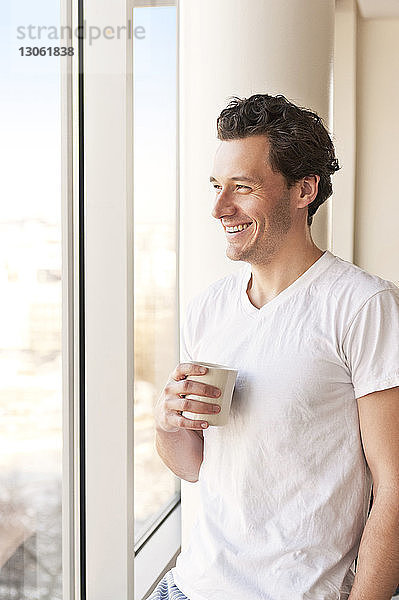 Lächelnder Mann trinkt Kaffee und schaut durchs Fenster