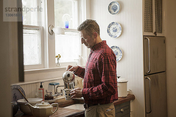 Seitenansicht eines Mannes  der Kaffee in einen Kaffeebecher gießt  während er zu Hause an der Küchentheke steht