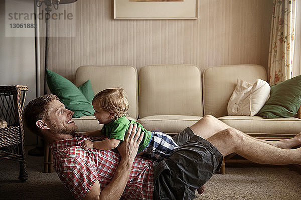 Seitenansicht eines Vaters  der zu Hause mit einem kleinen Jungen auf einem Teppich spielt