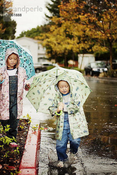 Geschwisterkind hält Regenschirm beim Gehen auf der Straße