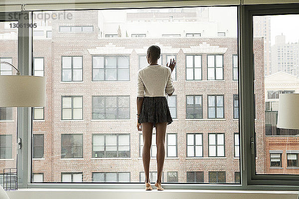 Frau in voller Länge steht zu Hause am Glasfenster
