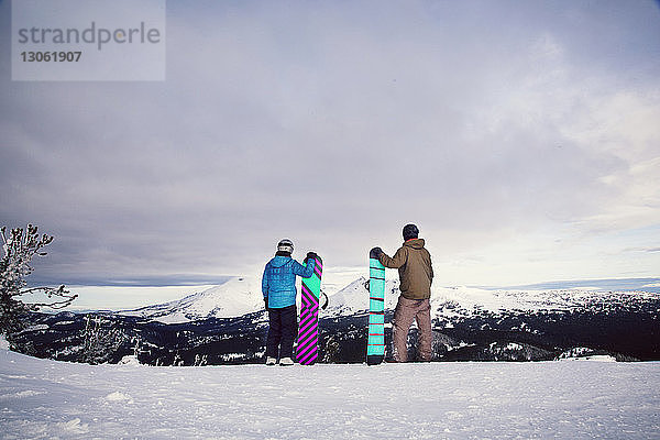 Freunde halten Snowboards in der Hand  während sie auf einem schneebedeckten Feld stehen