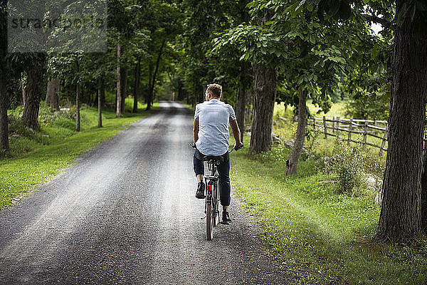 Rückansicht eines Fahrrad fahrenden Mannes auf einer Straße im Wald