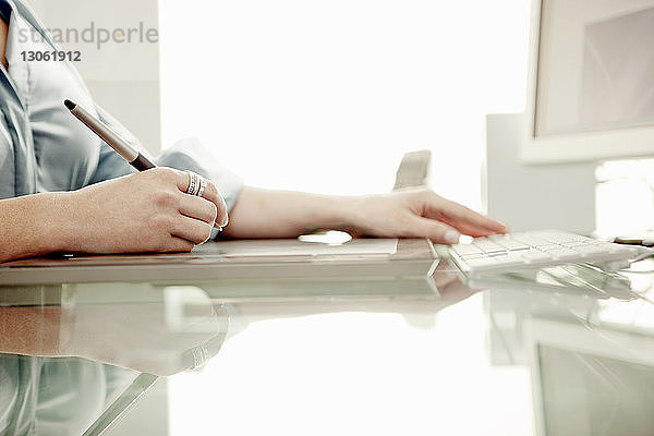 Beschnittenes Bild einer Geschäftsfrau mit digitalem Stift auf einem Bürotisch